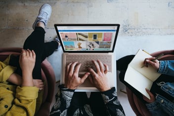 woman sitting crossed legged, man typing on a computer and woman writing in a notebook